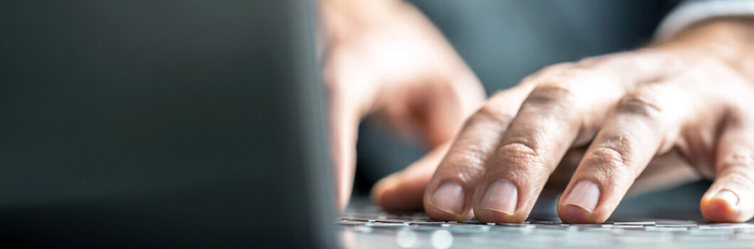 Low-angle view from the back of the computer of a businessman typing on a laptop computer keyboard.