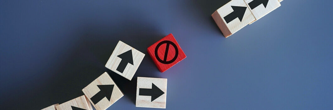 a line of blocks with arrows painted on them are interrupted by a block with the universal no sign painted on it.