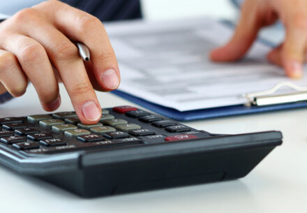 an auditor looks at forms and works on a calculator.
