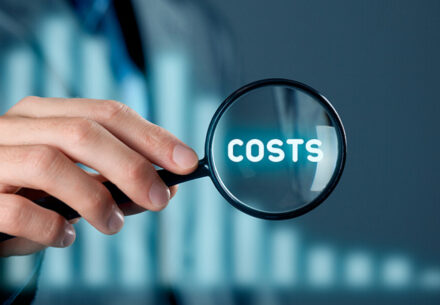 a businessman puts a magnifying glass over the word costs.