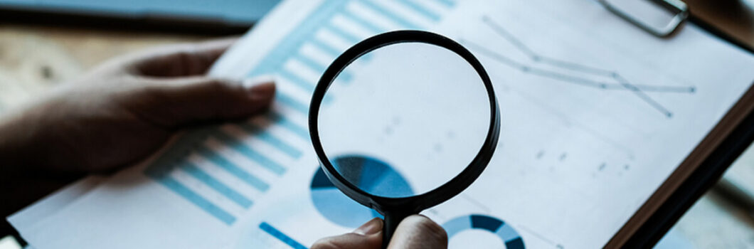 a person holds a magnifying glass to a financial report.