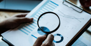 a person holds a magnifying glass to a financial report.