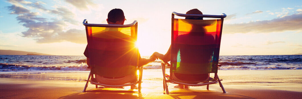 the silhouette of a happy couple resting on beach chairs by the ocean at sunset.