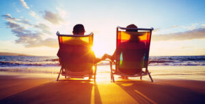 the silhouette of a happy couple resting on beach chairs by the ocean at sunset.