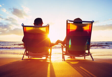 the silhouette of a happy couple resting on beach chairs by the ocean at sunset.