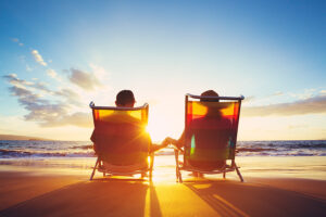 the silhouette of a happy couple resting on beach chairs by the ocean at sunset.