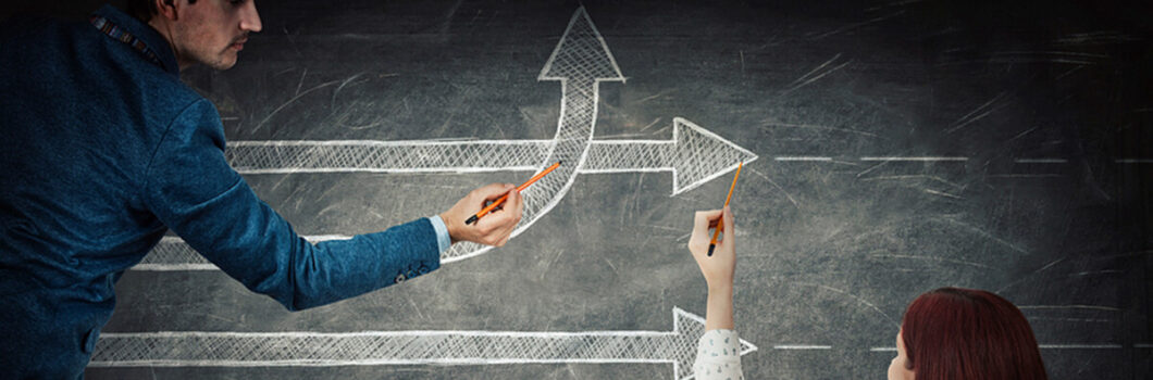 a man and a woman drawing divergent lines on a chalkboard.