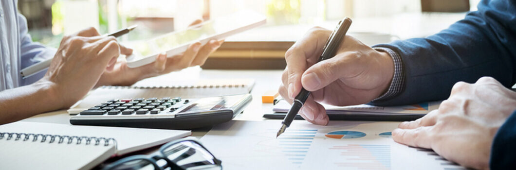 two businesspeople sit across a table from each other working on financial reports.