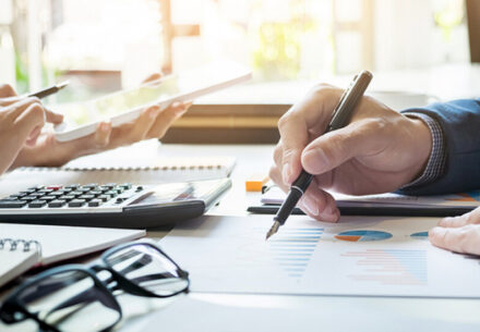 two businesspeople sit across a table from each other working on financial reports.